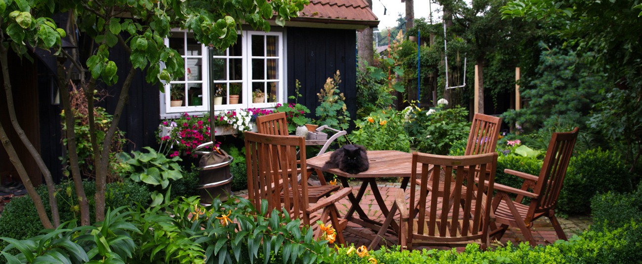 Geschützter Gartensitzplatz vor einem dunklen Gartenhaus, umgeben von üppiger Bepflanzung